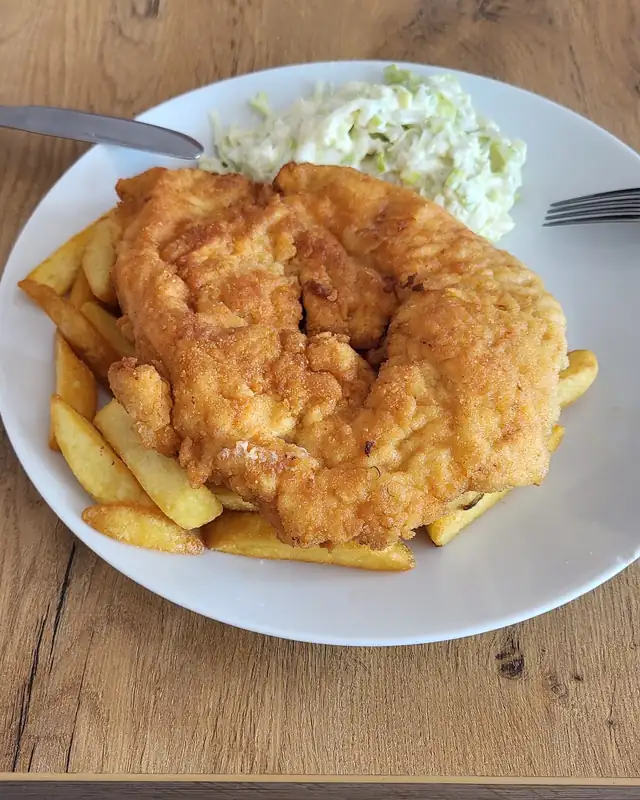 Kotlet z frytkami i surówką na białym talerzu
